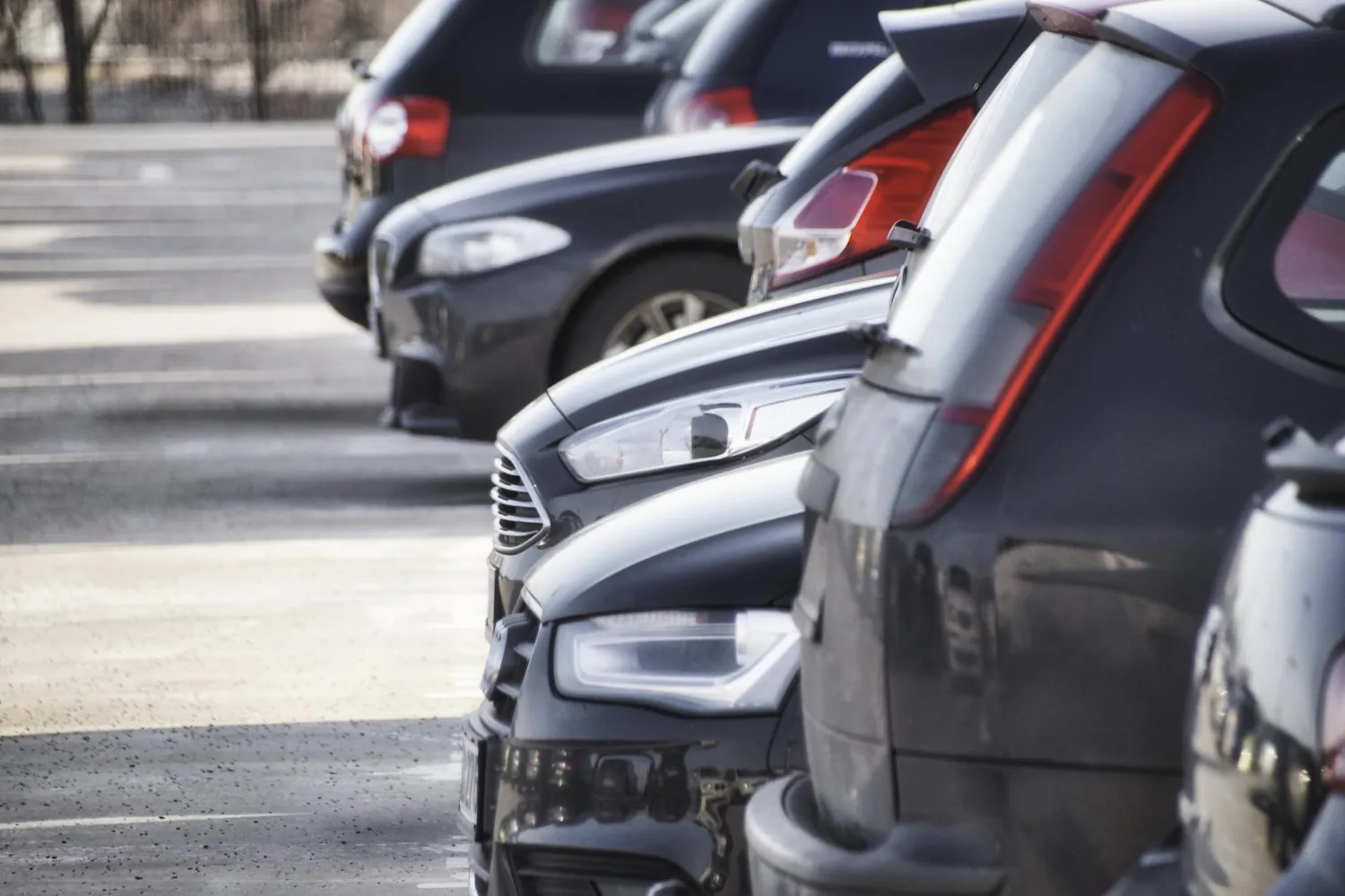 Mehrere eng geparkte Autos auf einem Parkplatz – Nahaufnahme der Stoßstangen und Rückleuchten, wo Parkschäden mit bekanntem Verursacher häufig entstehen.