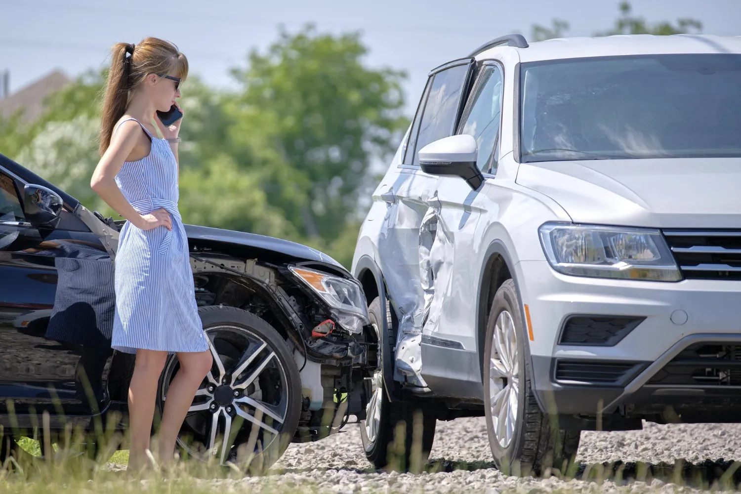 Frau telefoniert nach einem Verkehrsunfall neben einem Auto mit Frontschaden und einem SUV mit eingedrückter Seite – Unfall: was tun als Geschädigter?